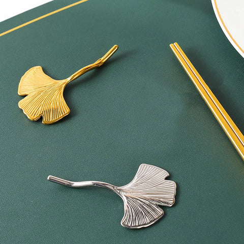 Gold and silver leaf-shaped chopstick rests on dark green surface, showcasing elegant modern tableware design