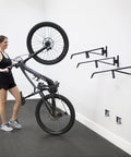 Woman installing Two Pack Wall Mount Bike Rack Set For Garage Storage Holds Two Mountain Bikes Up To 70 Lb Each No Lift Vertical Hanger