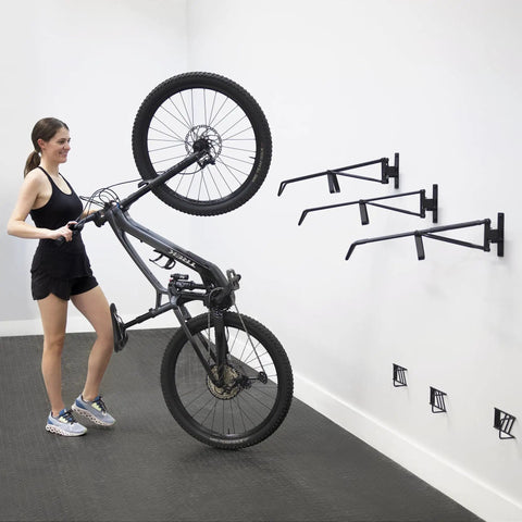 Woman installing Two Pack Wall Mount Bike Rack Set For Garage Storage Holds Two Mountain Bikes Up To 70 Lb Each No Lift Vertical Hanger