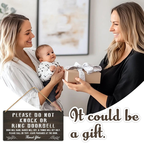 Two women exchanging a gift with a baby and the Please Do Not Ring Baby Sleeping Sign for Front Door hanging nearby.