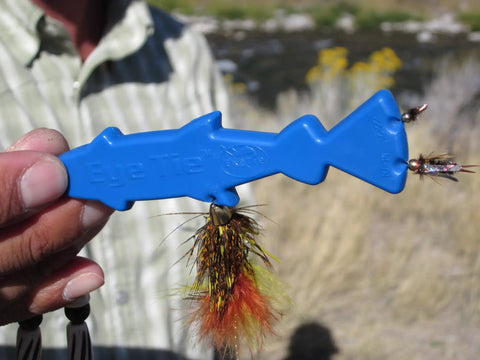 Hand holding blue Eye Tie Fly Threader With Magnetic 3 Funnel System For Hook Sizes 3 To 24 in outdoor setting.