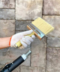 Hand holding a Deck Stain And Paint Brush 5 Inch Wide For Quick Decking And Surface Prep No Mess in front of a stone wall.