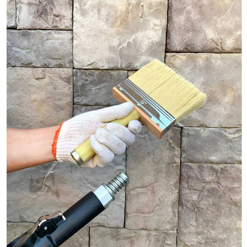 Hand holding a Deck Stain And Paint Brush 5 Inch Wide For Quick Decking And Surface Prep No Mess in front of a stone wall.