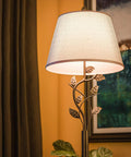 Close-up of rustic oil rubbed bronze floor lamp with leaf finial and gold tapered shade for living room, hallway, and bedroom ambience.