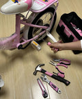 Using Pink Tool Set 218-Piece Home Improvement Kit For Women to repair a bike with tools spread on floor.