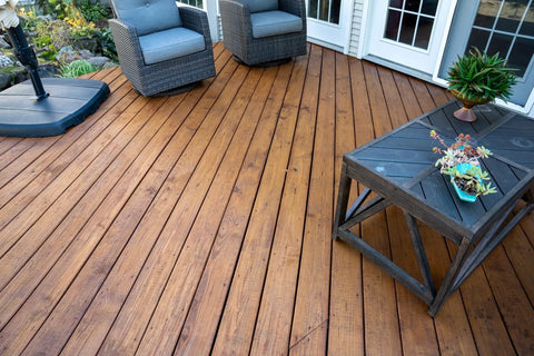 Heavy Duty Wood Stain And Sealer In One For Decks, 5 Gallon Semi Transparent Waterproof Coating In Light Walnut on a wooden deck with furniture.