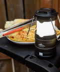 Pop Up IPX4 Water Resistant LED Lantern With 360 Degree Bright Light Four Modes Easy Fold Out Handle next to grilled food