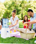 Family picnic with Compact Water Jug Dispenser Stand For Office Use Go To Hydration Station in the park, next to a picnic basket.