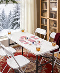 Heavy Duty 4ft Folding Table With Steel Legs set for cards, surrounded by chairs, in a cozy indoor setting with winter view