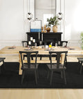 Dining room with wooden table, black chairs, and black rug on light wood floor.