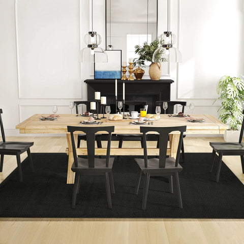 Dining room with wooden table, black chairs, and black rug on light wood floor.