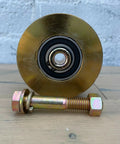 Badass 4 Inch Solid Gate Roller Wheel With Dual Bearing V Groove, Zinc Plated Gold Finish, 2500 Lbs Per Pair Capacity, Mounting Kit Included, Serious Grind Gear displayed with mounting bolt and nut.