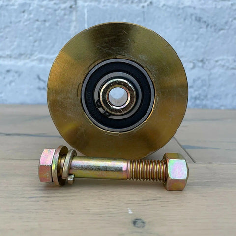 Badass 4 Inch Solid Gate Roller Wheel With Dual Bearing V Groove, Zinc Plated Gold Finish, 2500 Lbs Per Pair Capacity, Mounting Kit Included, Serious Grind Gear displayed with mounting bolt and nut.