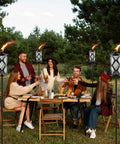Group of people dining outdoors surrounded by 4 Pack Gray Glass Outdoor Garden Torches 59 Inch Tall With Upgraded 16 Oz Citronella Fuel