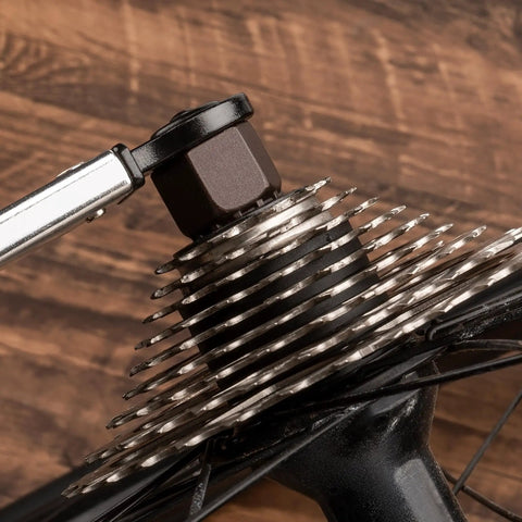 Close-up of bike cassette being serviced with Two In One Chain Whip And Lockring Tool For Cassettes on wooden background.
