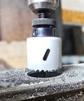 Maycraft hole saw bit in drill chuck; white housing with serrated cutting teeth cutting metal.