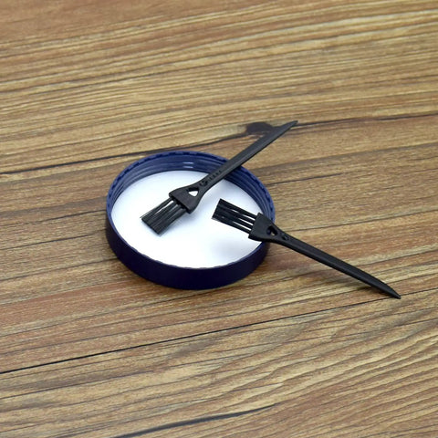 Two black scrapers on a white dish, part of the 17 Piece Herb Grinder Cleaning Kit With Scrapers Spoons Long And Short Brushes And Storage Box