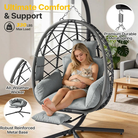 Woman sitting in grey Hanging Egg Chair With Adjustable Footrest And Stand For Indoor And Outdoor Use Wicker Swing Chair With Cushion, holding a cat.