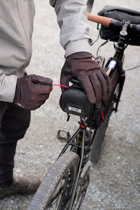 Cyclist adjusting waterproof under saddle seat pack for bike commuting and touring, recycled ripstop bag with adjustable saddle mount.