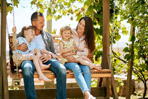Family enjoying quality time on a wooden swing in a lush garden setting, representing outdoor lifestyle.