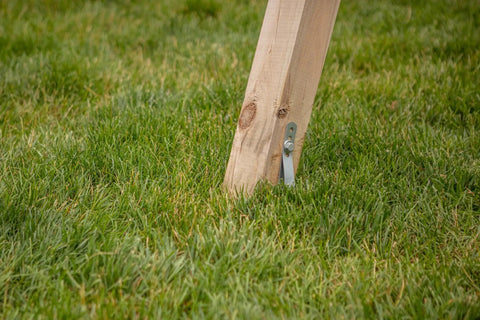 Wooden swing set leg anchored in grass using Playset Anchor Kit For Swing Sets Heavy Duty Ground Anchors That Keep Your Set Rock Solid Stationary And Safer For Outdoor Fun Easy Install Swing Set Hardware To Secure Play Equipment And Protect Your Kids