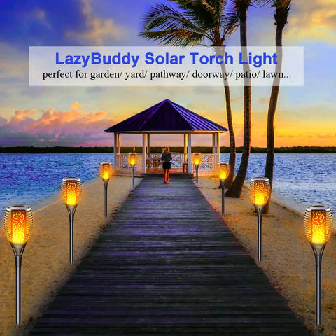 Sun Powered Solar Torch Lights Outdoor Flickering Flame 3 In 1 Detachable Hanging Lanterns No Wiring Auto On Off IP65 Waterproof Tiki Torches For Garden Path Patio Yard Decor 6 Pack illuminating a beach pathway towards a gazebo at sunset.