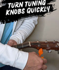 Guitar 3-in-1 tool (orange) clamped to headstock as a person winds strings on a wooden guitar.