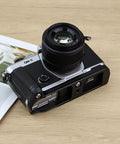 OM System OM 3 Hand Grip Camera Bracket With Arca Swiss Interface on table, showing textured leather grip and I/O access