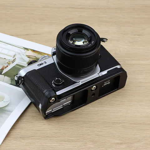 OM System OM 3 Hand Grip Camera Bracket With Arca Swiss Interface on table, showing textured leather grip and I/O access