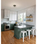 Modern kitchen with Hartland Flush Mount Ceiling Light in Noble Bronze With Seeded Glass Shade, white stools, and green cabinetry.