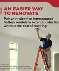 Man on a ladder installing a hardwired smoke detector in a home renovation, emphasizing safety features.