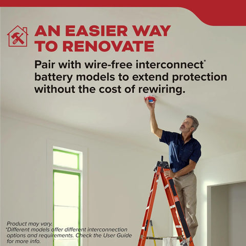 Man on a ladder installing a hardwired smoke detector in a home renovation, emphasizing safety features.
