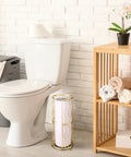 Gold Finish Standing Toilet Paper Holder With Three Roll Reserve next to a toilet in a bathroom with wooden shelf and towels