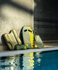 Poolside swim accessories including kickboard and fins next to a swimming pool in a sunlit indoor setting.