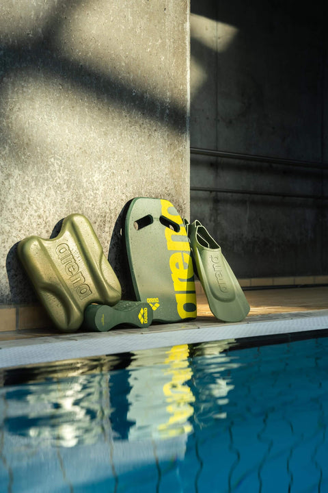 Poolside swim accessories including kickboard and fins next to a swimming pool in a sunlit indoor setting.