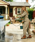 Pressure washer spray wand with hose used to rinse a blue car; front view of person in beige jumpsuit.