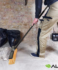 Real Deal Heavy Duty Push Broom With Long Handle Made To Crush Daily Grime On Smooth Floors Sweeps Sand Mud Leaves And Water Easy Without Breaking A Sweat In Bright Yellow 18 Inches Wide cleaning debris in a garage.