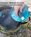 Hands washing a dish with soap over a 10L collapsible sink from You Gotta Have Camp Kitchen Cleanup Kit 6 Piece Set