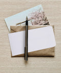 Photo of thick white blank letter envelopes 230x120mm bulk pack with pen and card on wooden table