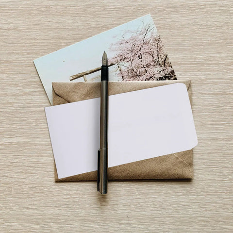 Photo of thick white blank letter envelopes 230x120mm bulk pack with pen and card on wooden table