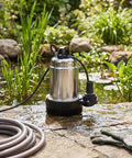 Cordless Submersible Water Pump 1003 GPH High Flow Battery Operated Drain Pump on stone by pond for garden irrigation use.