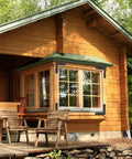 Rustic wooden cabin with large windows, two chairs on the porch, surrounded by trees