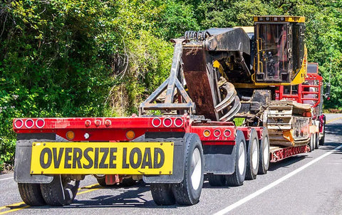 Two Pack 18x84 Oversize Load Sign for Trucks with Bungee Cord and Hook attached to a flatbed trailer carrying heavy machinery.