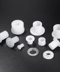 White plastic bushings and washers on a black surface, various sizes and shapes visible.