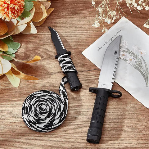 Decorative knife with black and white rope on a wooden surface, surrounded by flowers and a letter.