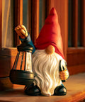 Garden Gnome Statue With Shovel And Lantern, Solar LED Lights That Glow At Night, Go To Outdoor Decor by window at dusk