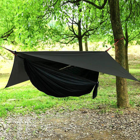 Durable Camping Hammock With Mosquito Net And Rain Fly For Outdoor Hiking And Backpacking set up between trees in a forest.