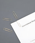 No Slip Paper Clips Set, 600 Count In Six Boxes Of 100 Each, One And Two Sevenths Inch By One Third Inch, on grey surface with paper.