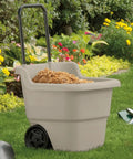 15 Gallon Resin Rolling Lawn And Utility Cart with retractable handle and 7 inch wheels, loaded with mulch in a garden setting