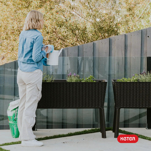 Person using Splendor 31.7 Gallon Raised Garden Bed With Self Watering Planter Box And Drainage Plug for growing plants outdoors